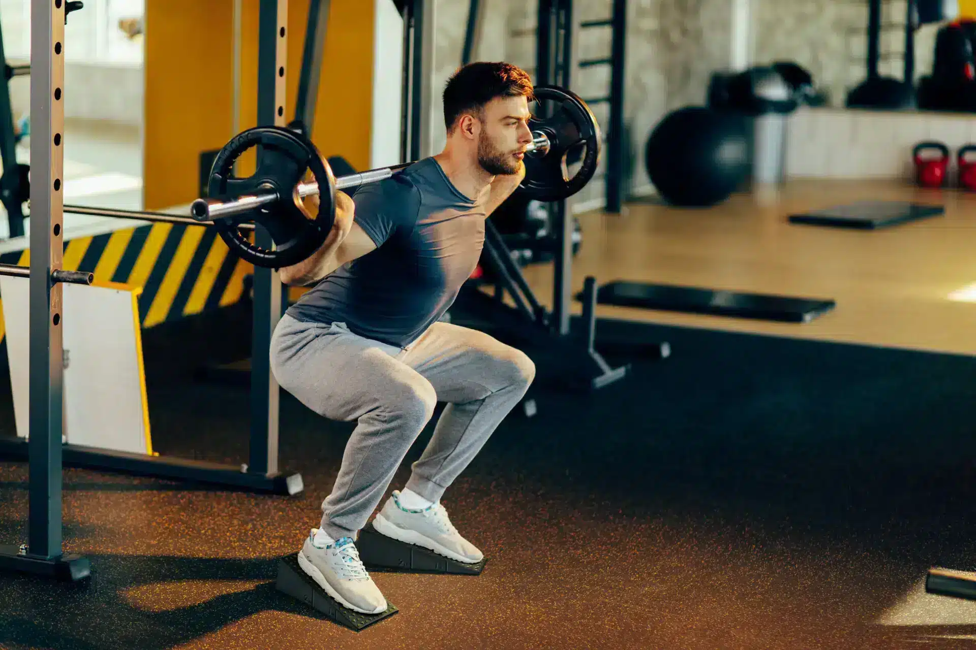 Man performing barbell squats using a slant board for improved form and balance.