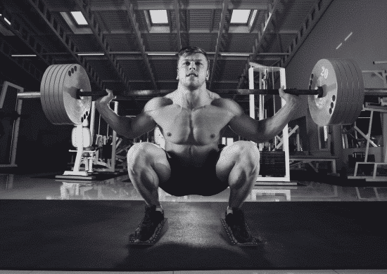 Male athlete performing deep squats with a heavy barbell using Flexelent squat wedges for improved form and mobility in a gym.